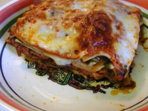 Homemade Lasagne Verdi featuring layers of green spinach pasta, rich Bolognese ragu, and melted golden-brown cheese on a white plate.