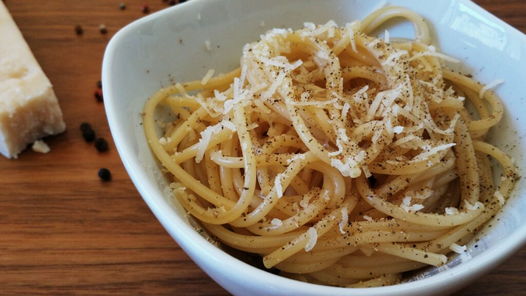 Cacio e Pepe Pasta served in a bowl with grated Pecorino Romano and cracked black pepper