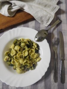 Plated orecchiette with broccoli rabe and sausage garnished with grated cheese and red pepper flakes.