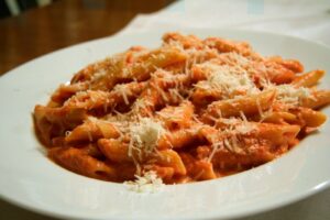 Penne alla Vodka served in a white bowl topped with fresh basil and grated Parmesan.